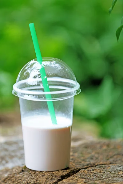 Plastic beker van milkshake op groene achtergrond, buitenshuis — Stockfoto