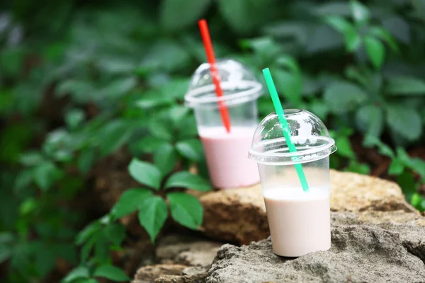 Plastic bekers van milkshake op groene achtergrond, buitenshuis — Stockfoto