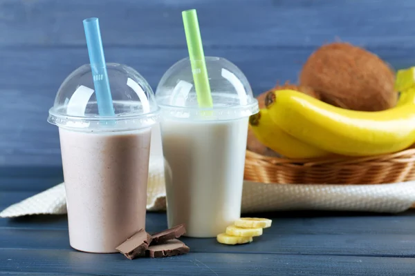 Plastic cups of milkshake with banana on color wooden background — Stock Photo, Image