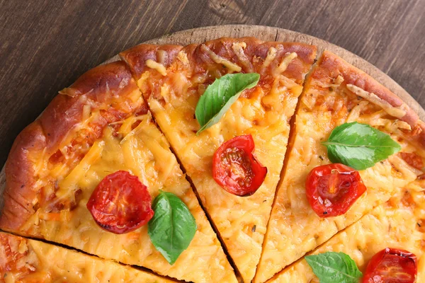 Segmenten van smakelijke kaas pizza met basilicum en cherry tomaten op tafel close-up — Stockfoto