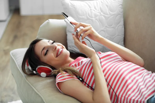 Женщина слушает музыку в наушниках, лежа на диване в комнате — стоковое фото