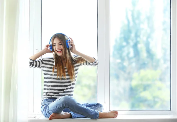 Woman listening music in headphones on windowsill background