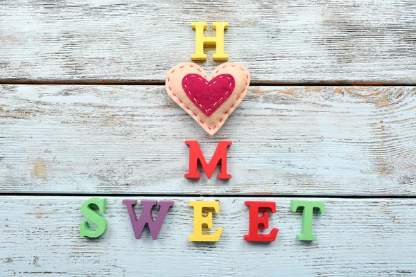 Decorative letters forming words SWEET HOME with heart on wooden background — Stock Photo, Image