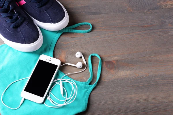 Teléfono móvil y auriculares con camiseta y zapatos en mesa de madera, primer plano —  Fotos de Stock