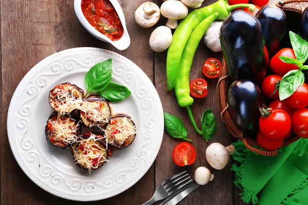 Dish of eggplant with cherry tomatoes and cheese in white plate on wooden table, top view — Stock Photo, Image