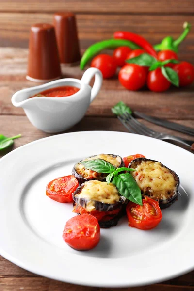 Dish of eggplant with cherry tomatoes and cheese in white plate on wooden table, closeup — Stock Photo, Image