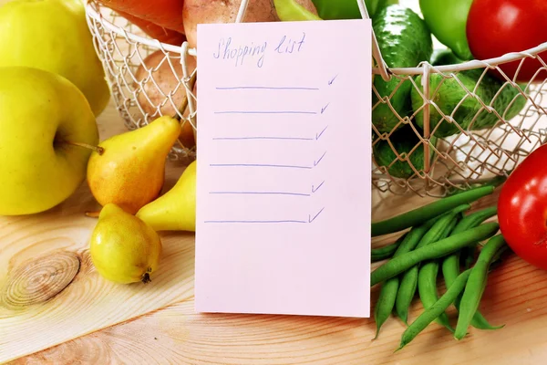 Haldy ovoce a zeleniny s nákupní seznam na stole zblízka — Stock fotografie