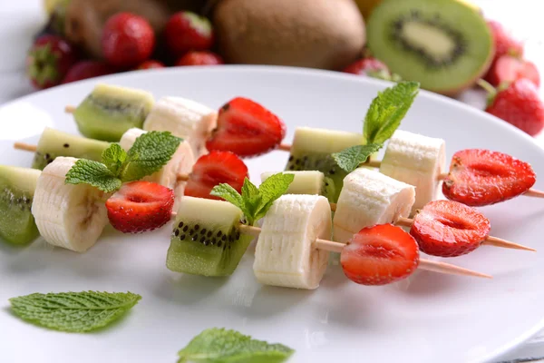 Frutta fresca su spiedini in piatto sul tavolo, primo piano — Foto Stock