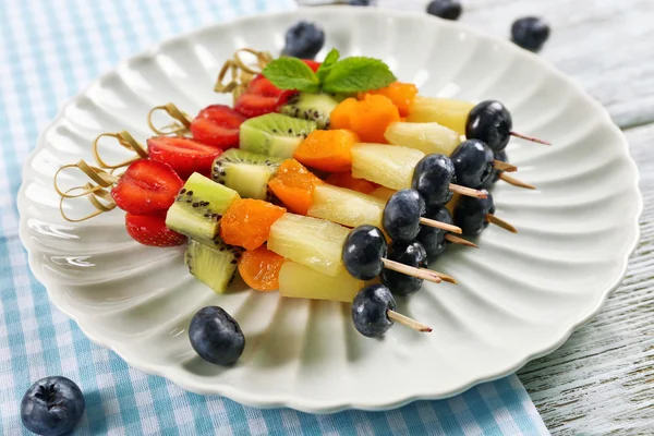 Frutta fresca su spiedini in piatto sul tavolo, primo piano — Foto Stock