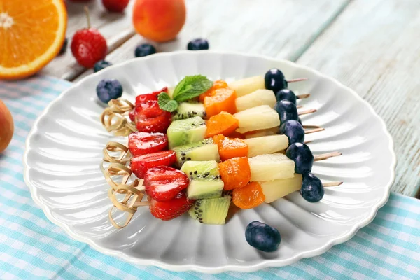 Fresh fruits on skewers in plate on table, closeup