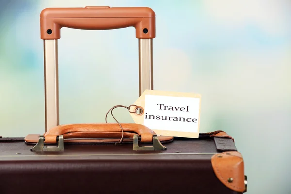 Suitcase with TRAVEL INSURANCE label on light blurred background — Stock Photo, Image