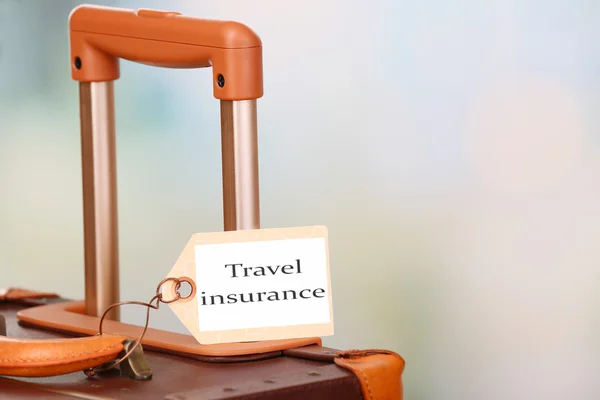 Suitcase with TRAVEL INSURANCE label on light blurred background — Stock Photo, Image