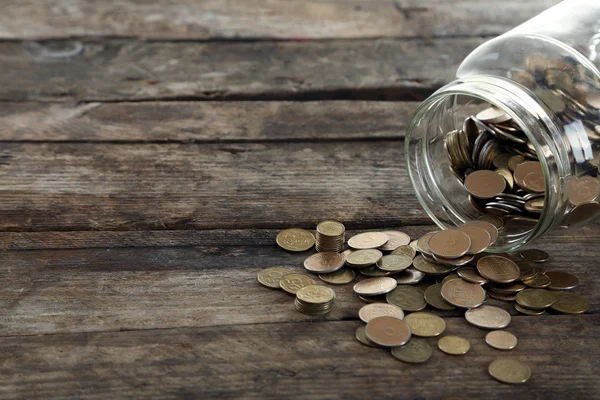 Coins in money jar on wooden background