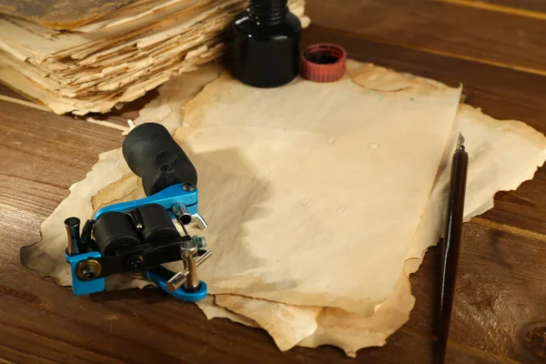 Máquina para tatuagem com papel velho e garrafa de tinta na mesa de close-up — Fotografia de Stock