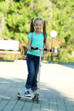 Küçük kız parkta scooter üzerinde sürme