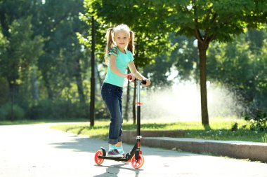 Küçük kız parkta scooter üzerinde sürme