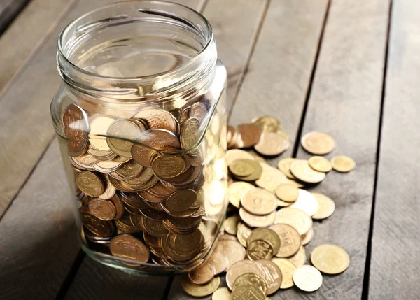 Glasgefäß mit Münzen auf Holzgrund — Stockfoto