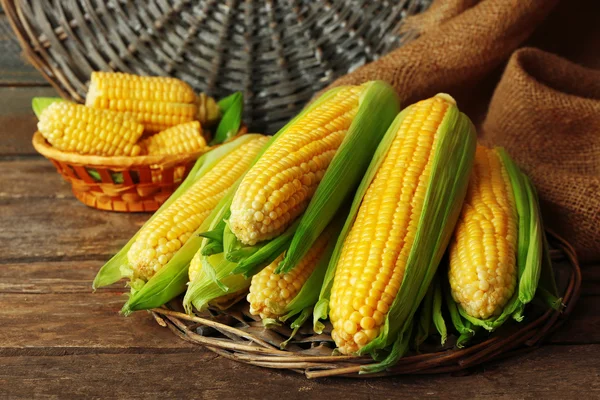 Fresh corn on cobs on wicker mat on wooden table, closeup — Stock Photo, Image