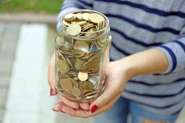 Woman holding money jar with coins outdoors