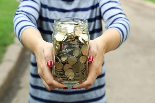 Mujer sosteniendo el frasco de dinero con monedas al aire libre —  Fotos de Stock