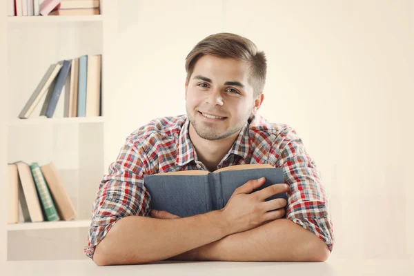 Young man reading book at table in room — Stock Photo, Image