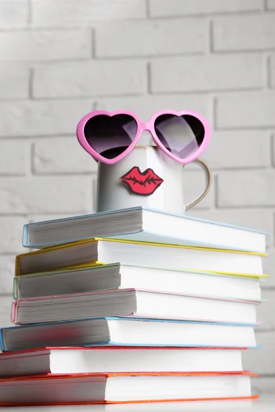 Boeken en cup met lippen op houten tafel op bakstenen muur achtergrond — Stockfoto