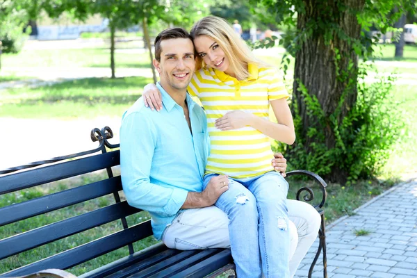 Junge schwangere Frau sitzt mit Mann auf Bank im Park — Stockfoto