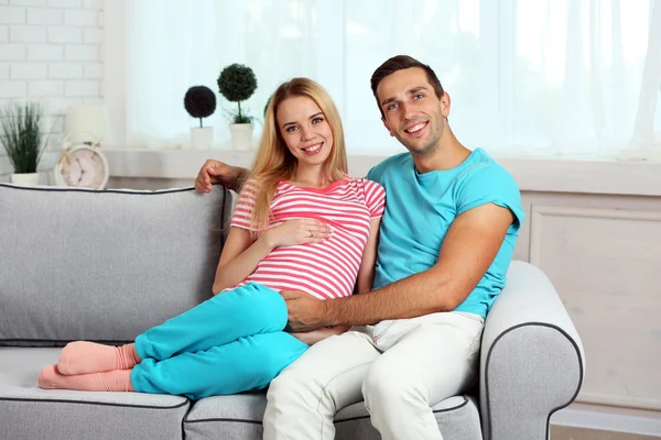 Jonge zwangere vrouw met echtgenoot op de bank in de kamer — Stockfoto