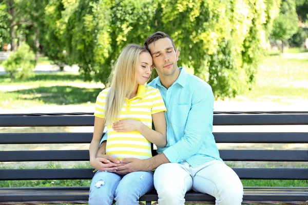 Νεαρή έγκυο γυναίκα με άντρα που κάθεται σε παγκάκι στο πάρκο — Φωτογραφία Αρχείου