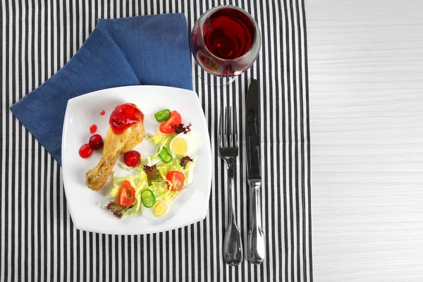 Πιάτο πόδι ψημένο κοτόπουλο και σαλάτα λαχανικών σε λευκή πινακίδα με ποτήρι κρασί στο τραπέζι με χαρτοπετσέτα, κάτοψη — Φωτογραφία Αρχείου