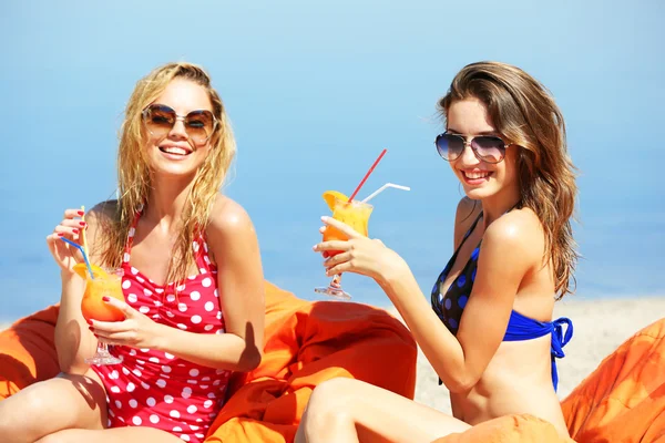 Twee jonge meisjes cocktail genieten op zak zetels op strand in de zomer — Stockfoto