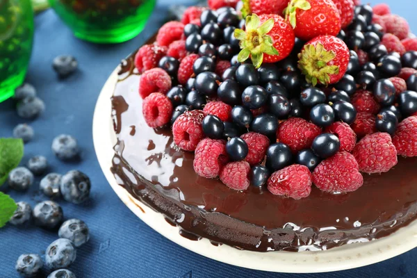 Delicioso pastel de chocolate con bayas de verano en mantel azul, primer plano — Foto de Stock