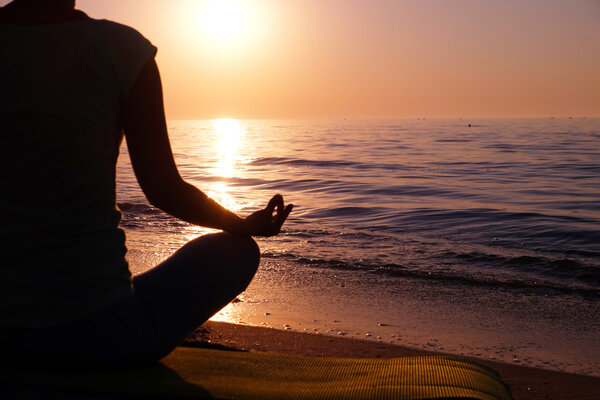 Young healthy woman practicing yoga on the beach at sunset