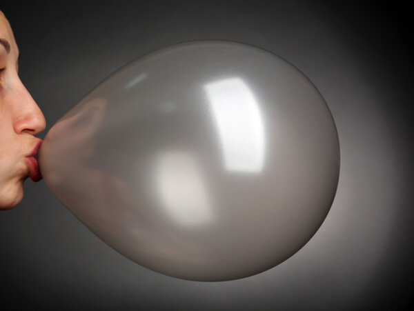 Young woman inflating balloon on gray background