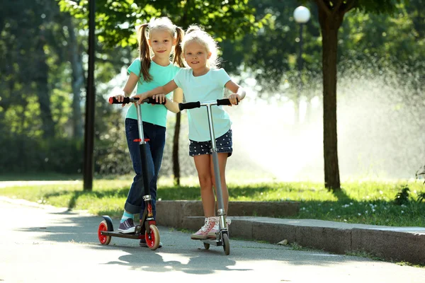 Small girls riding on scooters in park — Stock Photo, Image