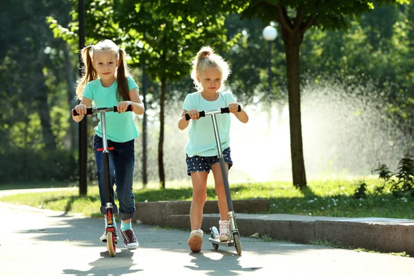Malé dívky, jízda na skútrech v parku — Stock fotografie