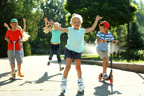 Niños montados en scooters y patines en el parque —  Fotos de Stock