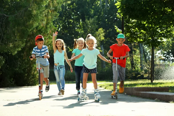 Children riding on scooters and roller skates in park — Stock Photo, Image