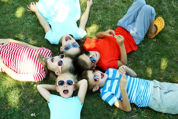 Щасливі активні діти лежать на зеленій траві в парку — стокове фото