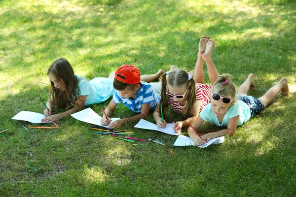 Happy active children lying on green grass and drawing in park — Stock Photo, Image