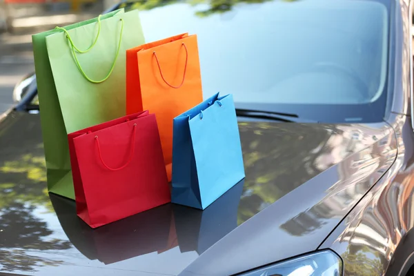 Sacos de compras brilhantes no capô do carro ao ar livre — Fotografia de Stock