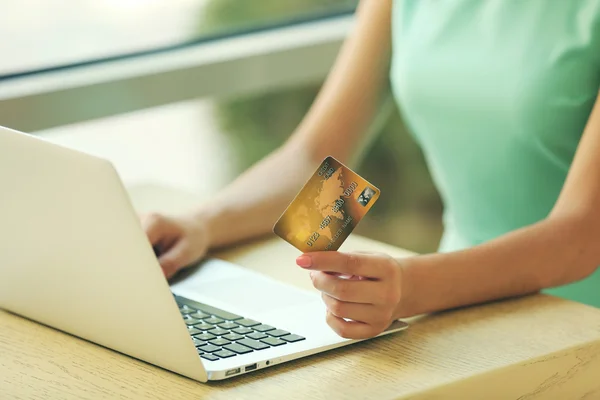 Mãos femininas segurando cartão de crédito com laptop na mesa de perto — Fotografia de Stock