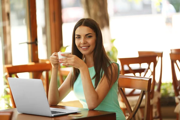 Hermosa mujer joven con ordenador portátil en la cafetería — Foto de Stock