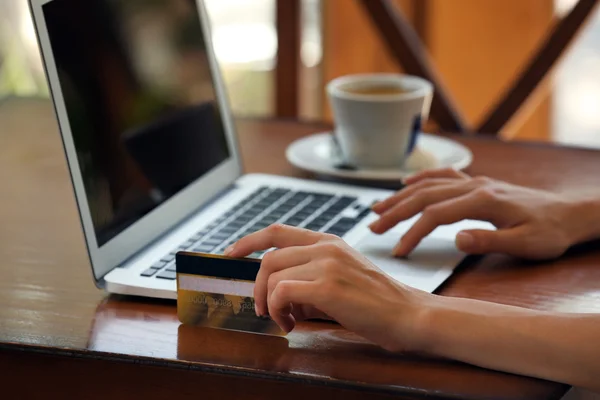 Mãos femininas segurando cartão de crédito com laptop na mesa de perto — Fotografia de Stock