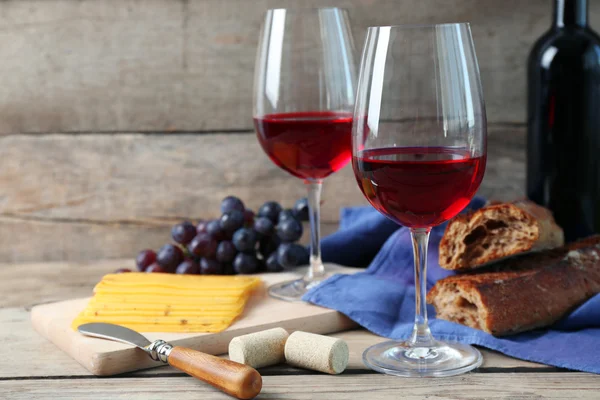 Still life of wine, grape, cheese and bread on rustic wooden background