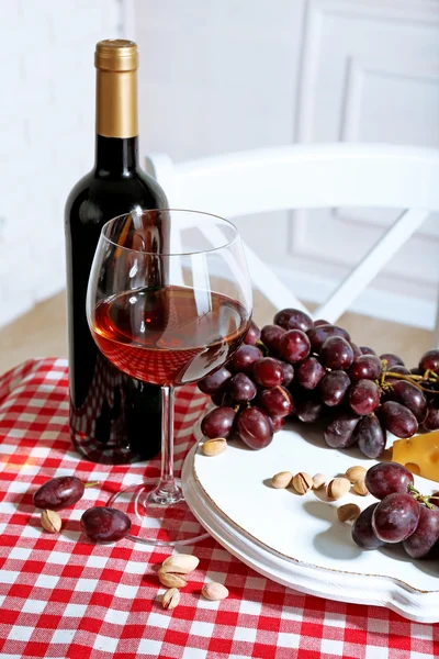 Červené hroznové víno a sýr se skleněnou lahví vína na světlém interiéru pozadí — Stock fotografie