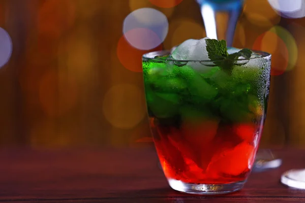 Glass of cocktail with ice on blurred lights background — Stock Photo, Image