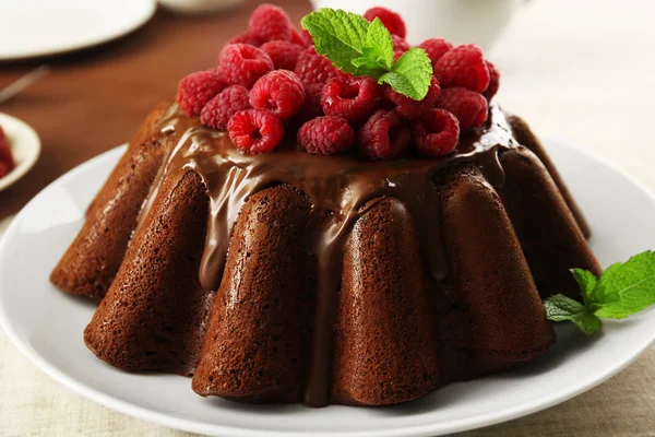 Tasty chocolate muffin with glaze and raspberries on table close up — Stock Photo, Image