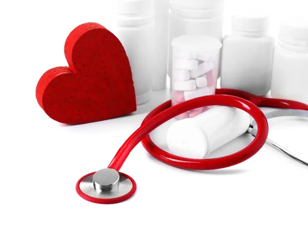 Medical stethoscope with bottles of pills and red heart isolated on white — Stock Photo, Image