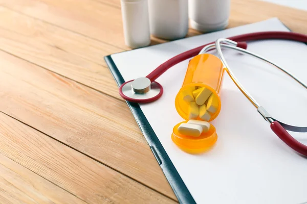 Medical stethoscope with clipboard and pills on wooden table close up — Stock Photo, Image